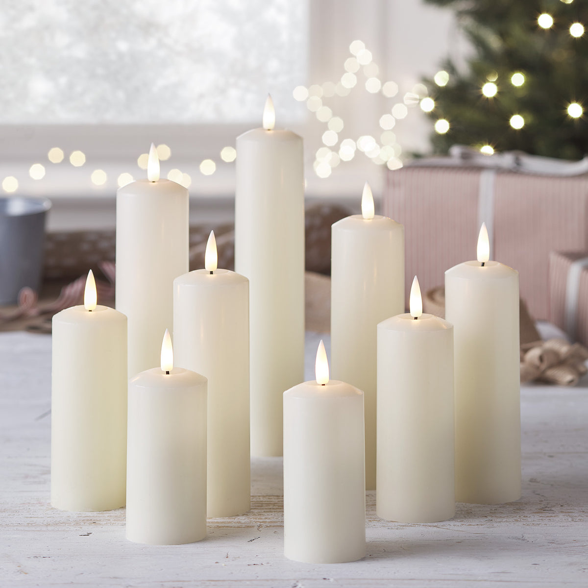 Neun brennende LED Echtwachskerzen auf weißem Tisch mit Weihnachtsdeko im Hintergrund