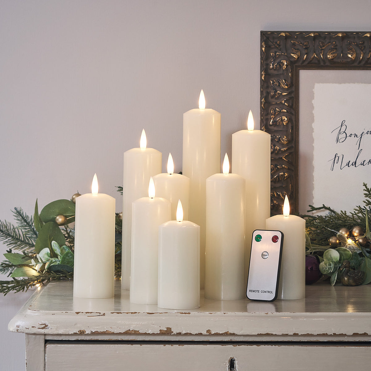 Neun brennende LED Echtwachskerzen mit Fernbedienung auf weißem Tisch mit Weihnachtsdeko