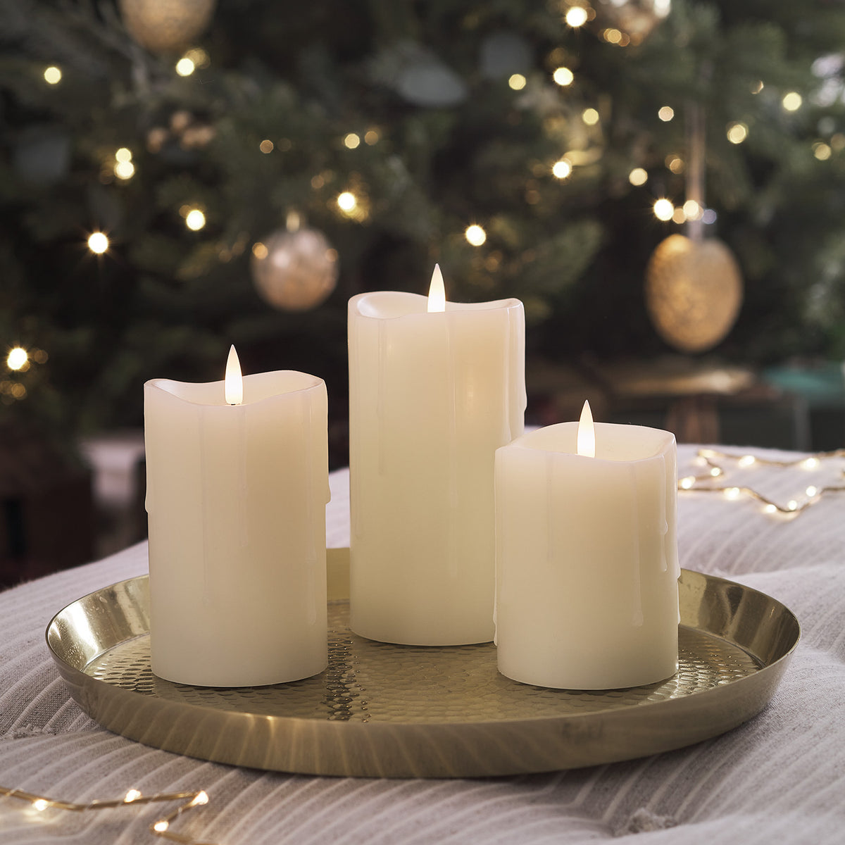 LED Stumpenkerzen mit warmweißem Licht auf goldenem Tablett vor Weihnachtsbaum mit Kugeln