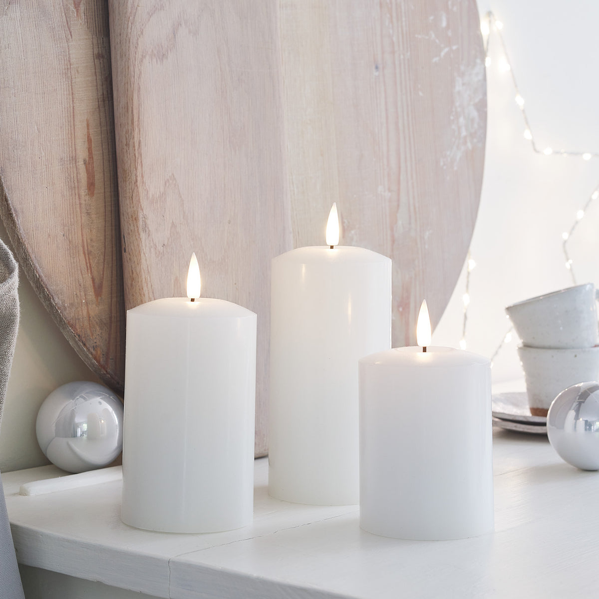 Drei brennende weiße LED Stumpenkerzen auf weißem Tisch mit Dekoration aus Holz und Keramik