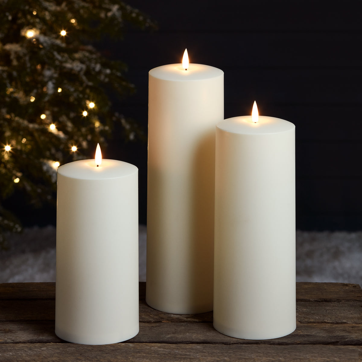 Drei brennende LED-Kerzen vor dunklem Hintergrund mit Lichterkette