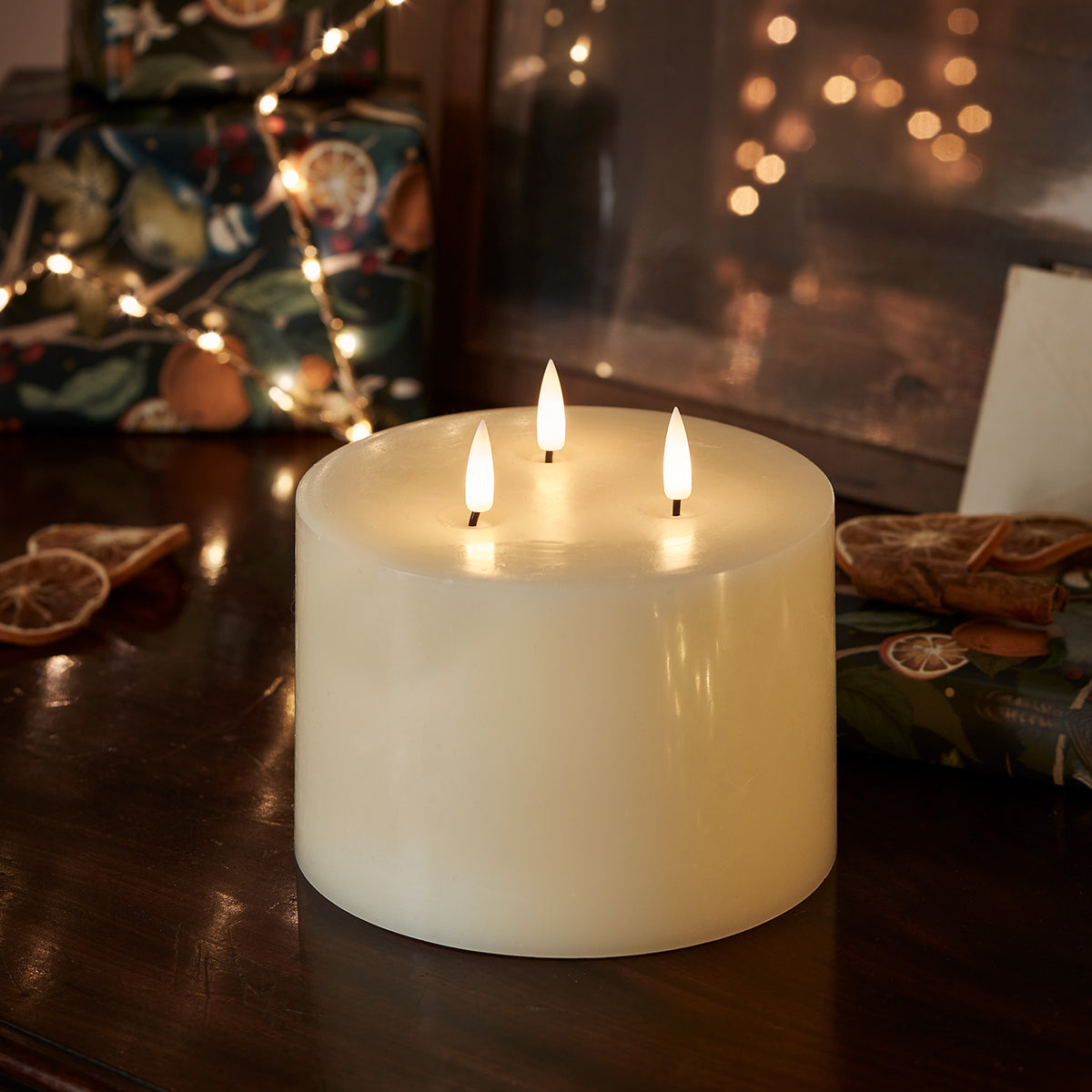 Dreidochtige LED-Kerze mit warmem Licht vor weihnachtlicher Dekoration