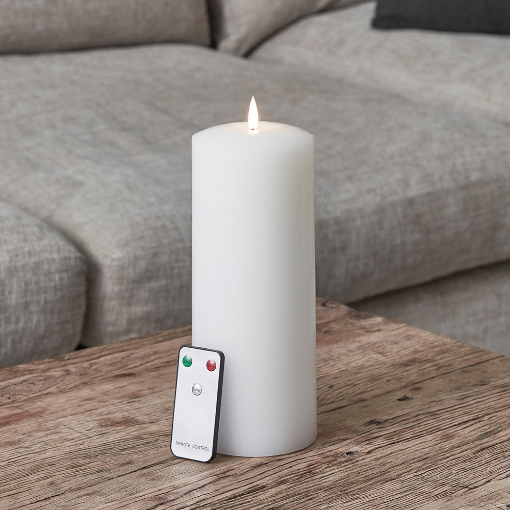 Weiße LED Stumpenkerze mit Fernbedienung auf Holztisch vor grauem Sofa