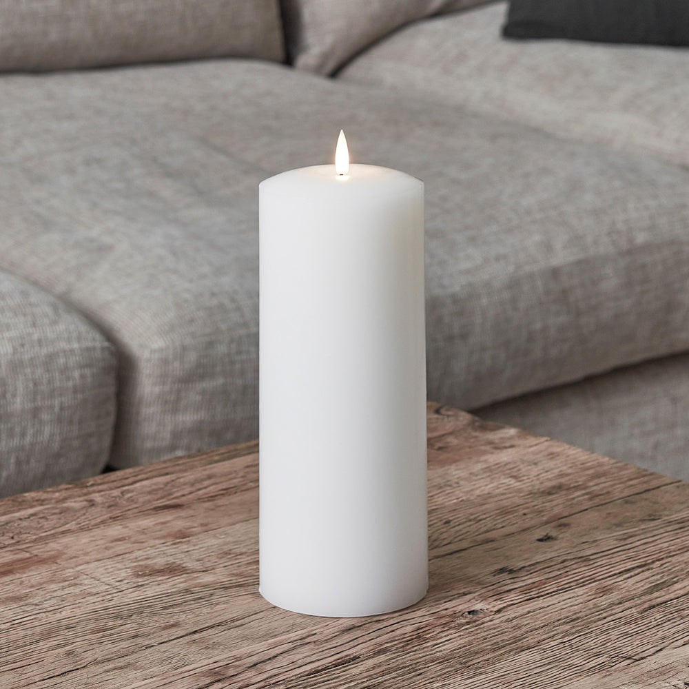 Weiße breite LED Stumpenkerze aus Echtwachs auf Holztisch vor grauem Sofa