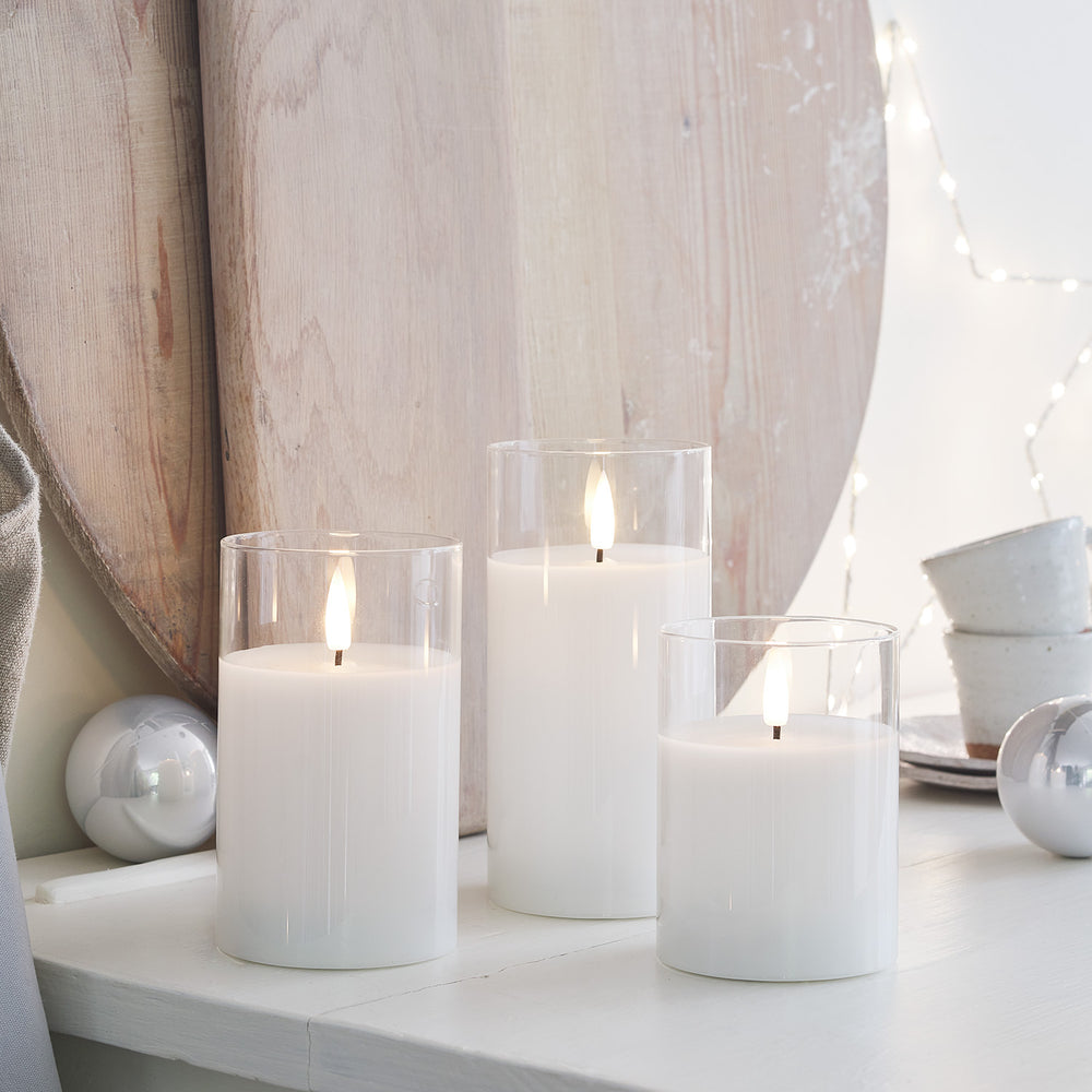LED-Kerzen Trio vor Holzbrett mit Weihnachtsdeko und silbernen Kugeln