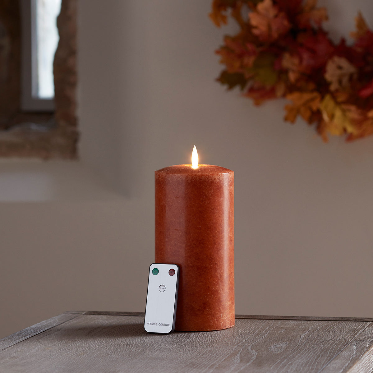 Orangefarbene LED-Kerze aus Echtwachs mit Fernbedienung auf Holztisch vor herbstlicher Deko