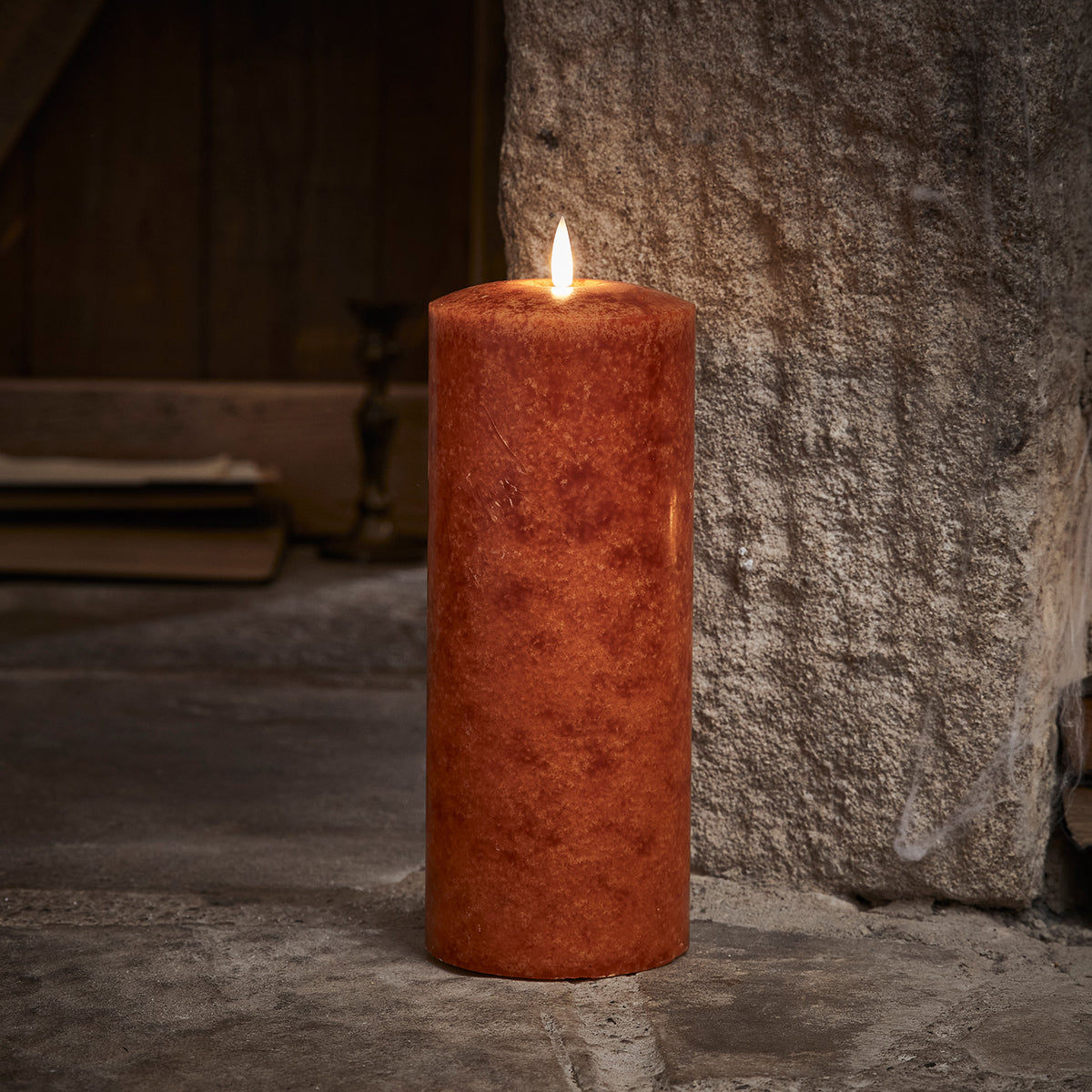 Leuchtende orangefarbene LED Stumpenkerze mit Fernbedienung auf Steinboden
