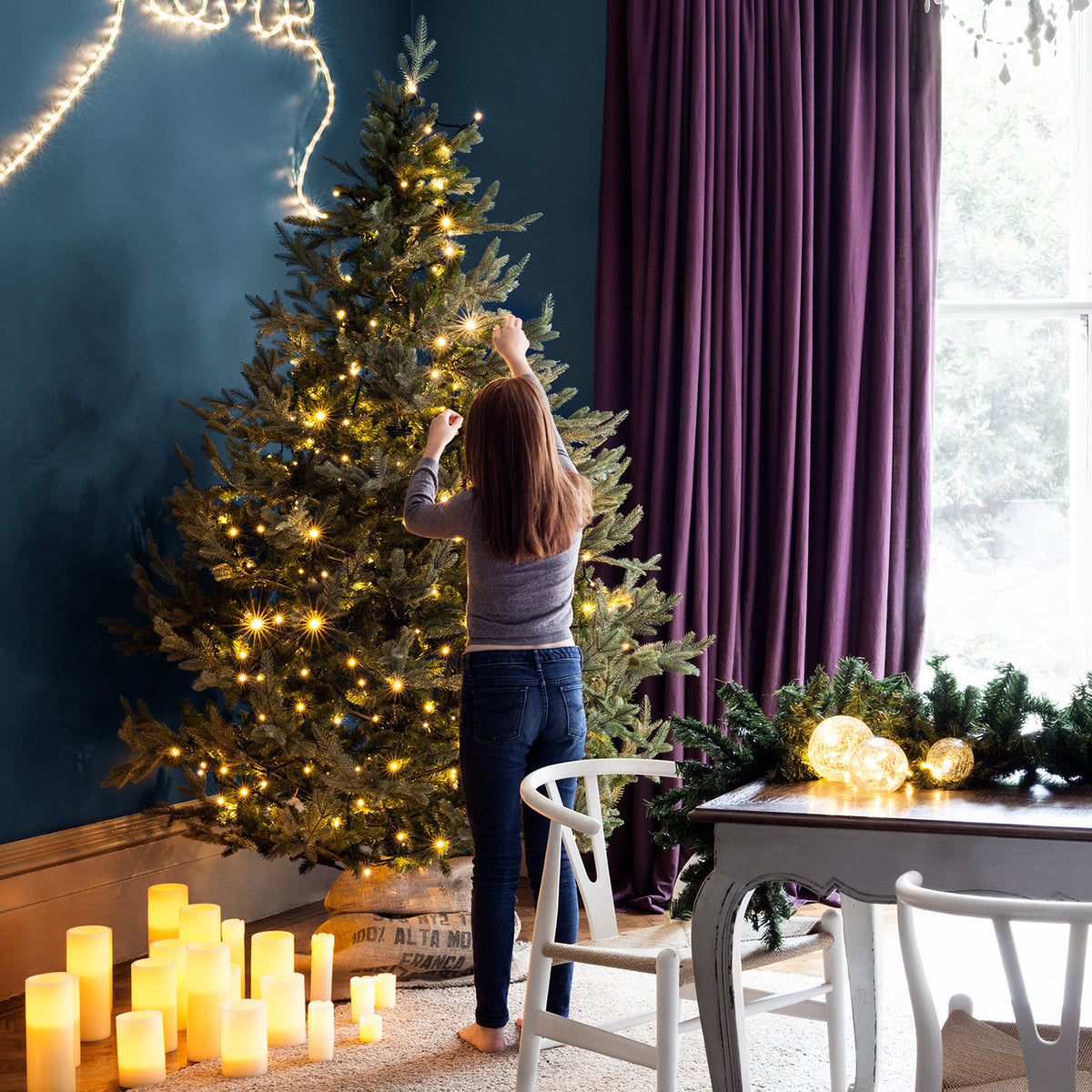 Frau schmückt Weihnachtsbaum mit warmweißen LED-Lichtern im Wohnzimmer