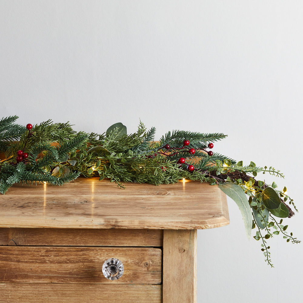 Weihnachtsgirlande mit roten Beeren und warmweißen Lichtern auf Holzkommode