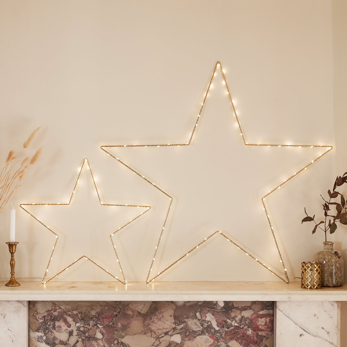 Zwei goldene Osby LED Sterne in verschiedenen Größen auf Kaminsims mit Kerzen und Deko