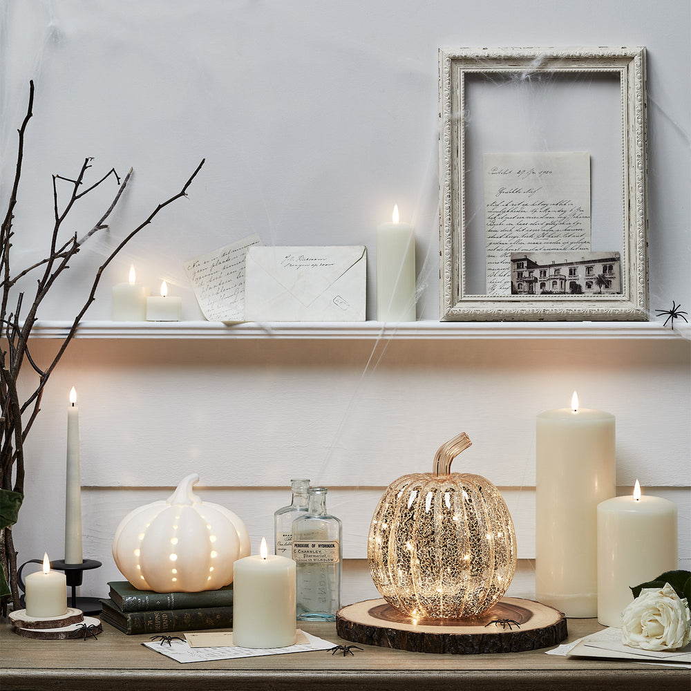 Herbstliche Dekoration mit weißen LED-Kerzen, zwei Kürbissen und Vintage-Briefen auf Holzbrett