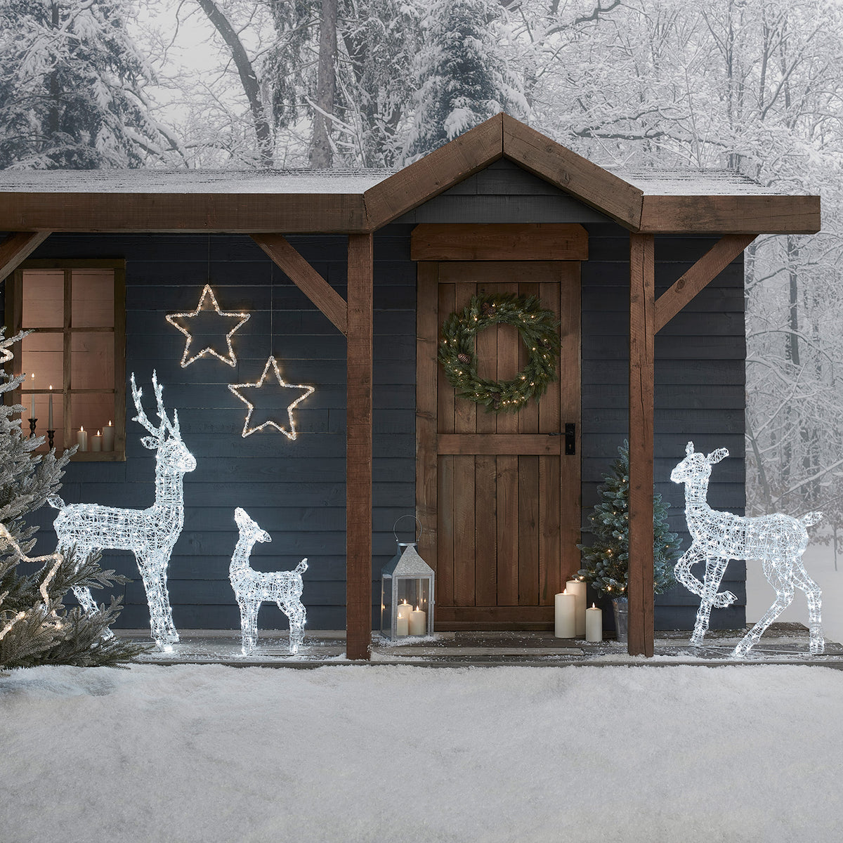 Weihnachtliche Rentierfamilie aus weißen LED-Lichtern vor Holzhütte mit Kranz und Kerzen