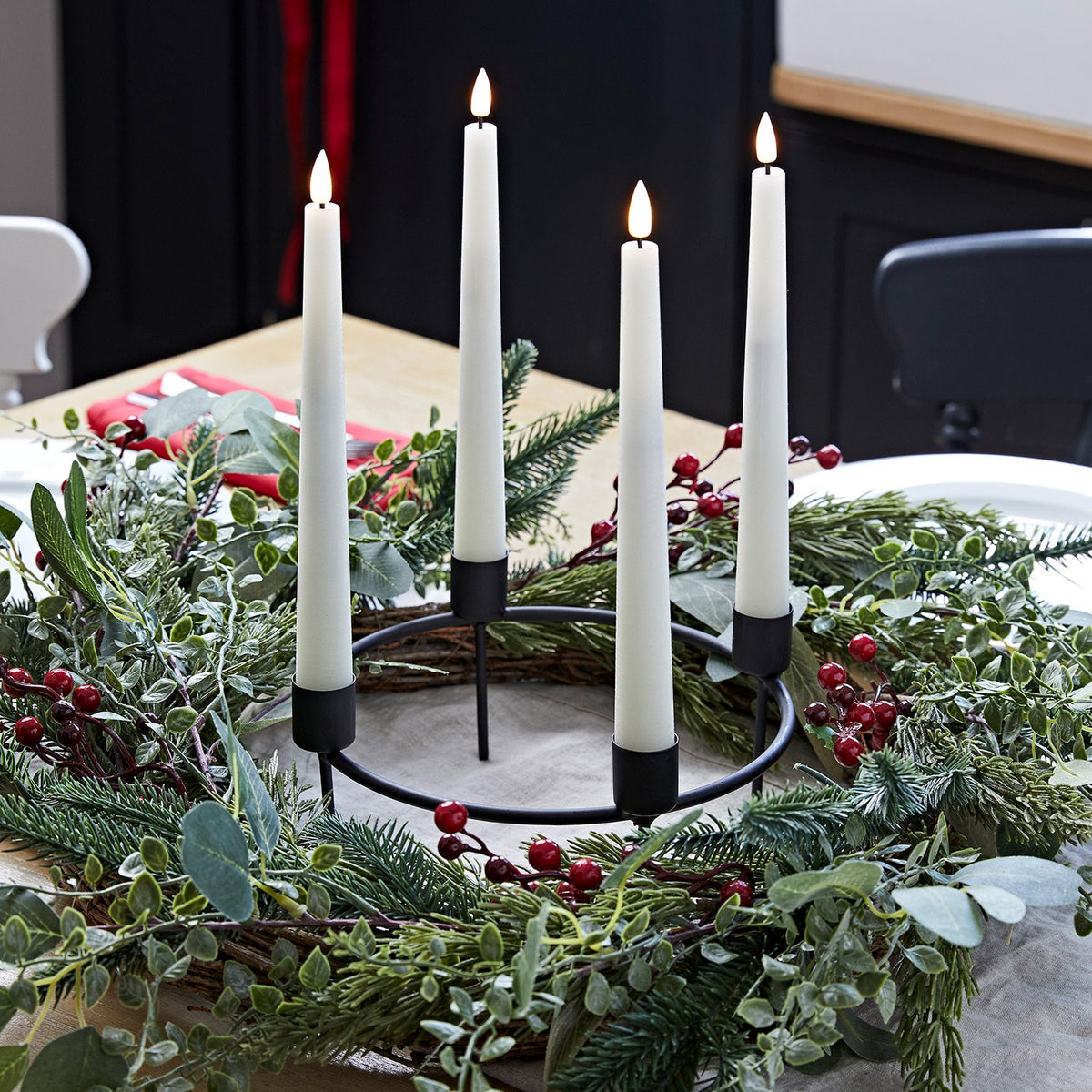 Adventskranz mit grünen Zweigen und roten Beeren, schwarzer Kerzenhalter mit vier weißen LED-Stabkerzen