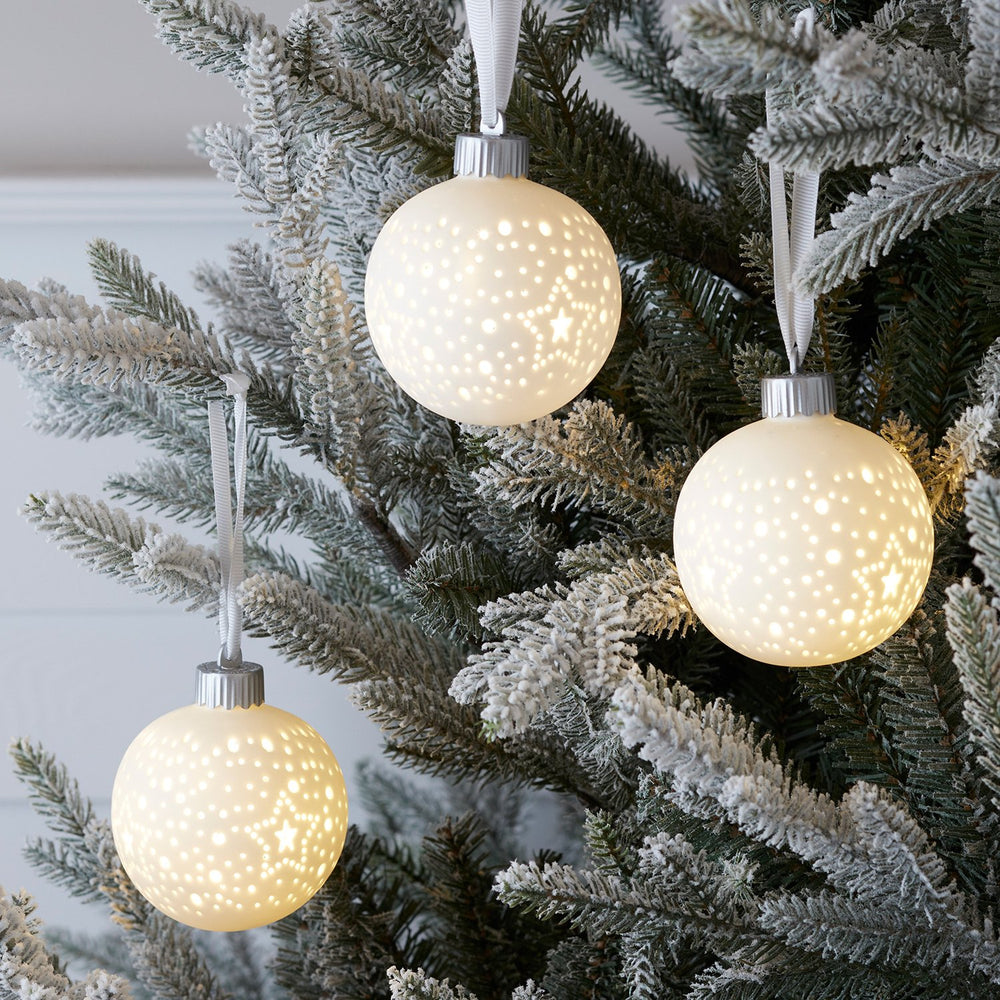 Drei leuchtende Keramik Weihnachtskugeln mit Stern- und Punktmuster an Tannenzweigen hängend