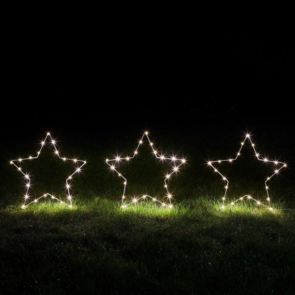 Drei leuchtende Micro LED-Sterne nebeneinander auf Gras bei Dunkelheit