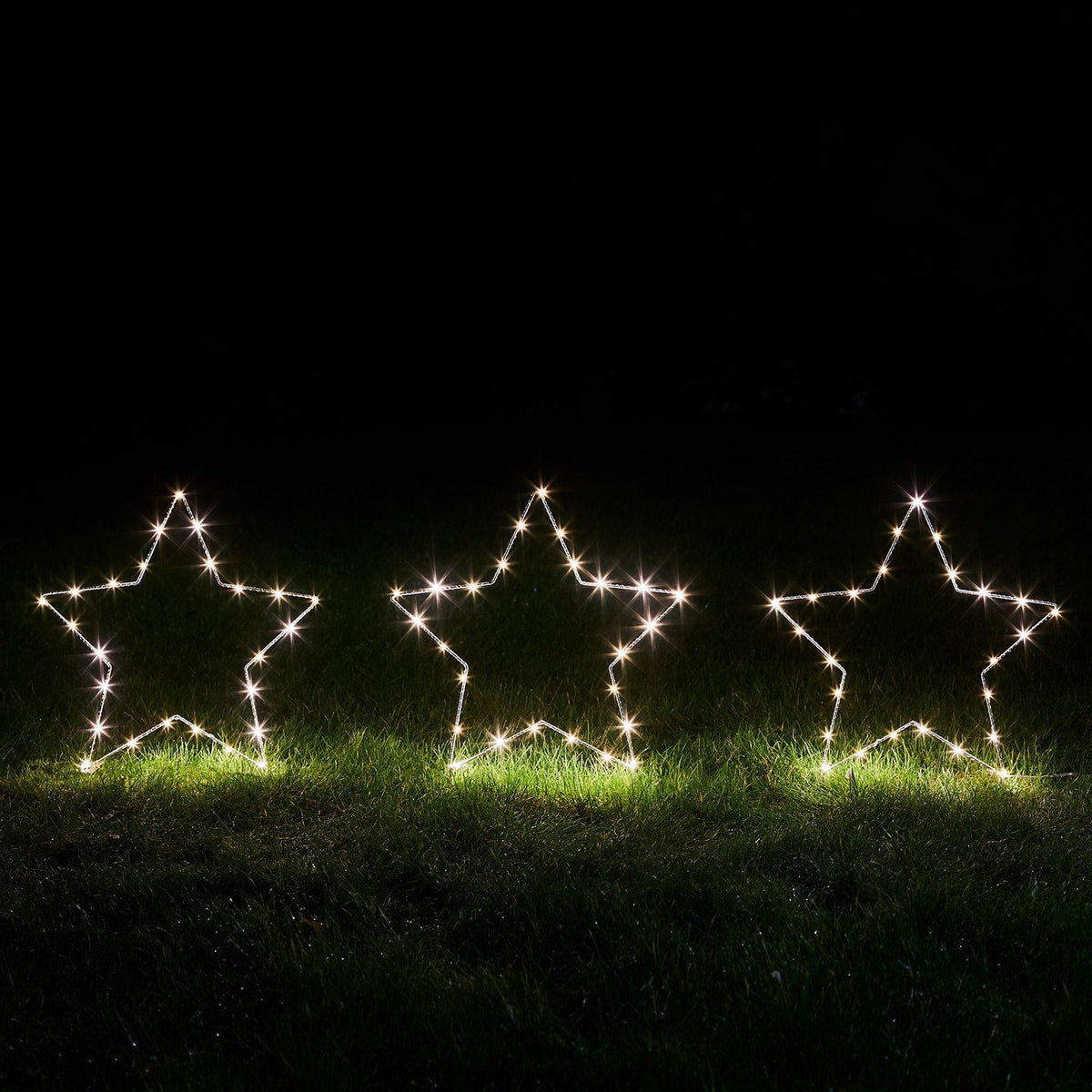 Drei leuchtende Stern-Stableuchten mit warmweißen Micro-Lichtern auf Rasen bei Nacht