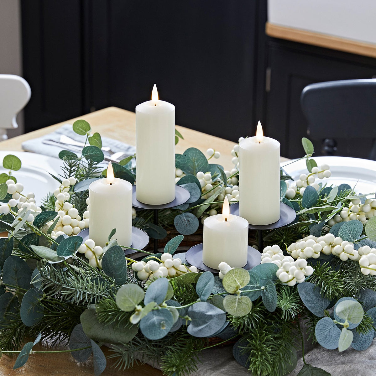 Kerzenständer mit vier weißen Stumpenkerzen in grünem Adventskranz auf gedecktem Holztisch
