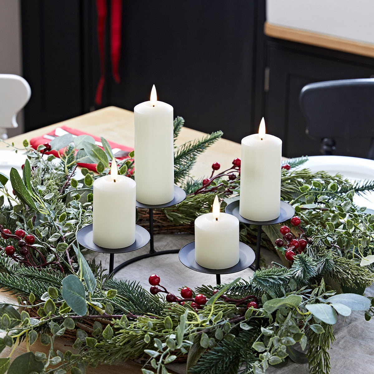 Adventskranz mit grünem Kunstlaub und roten Beeren, schwarzer Kerzenhalter mit vier weißen LED-Kerzen