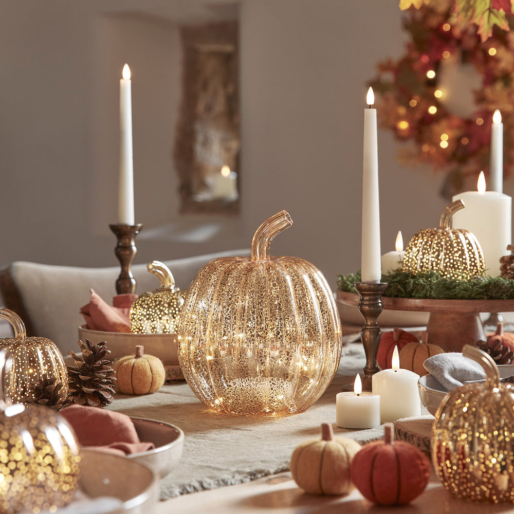 Herbstliche Tischdeko mit leuchtenden Glas-Kürbissen, Kerzen und kleinen Wollkürbissen
