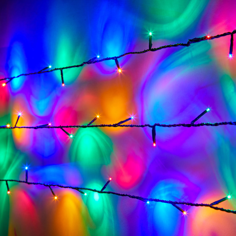 Nahaufnahme bunte LED-Lichterkette mit grünem Kabel vor farbig leuchtendem Hintergrund