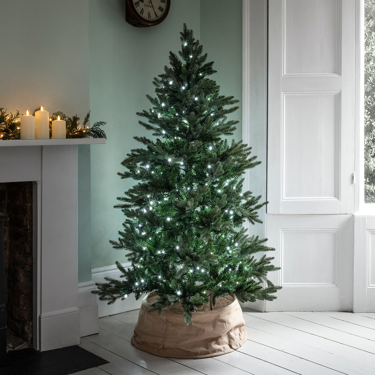 Weihnachtsbaum mit weißer LED-Lichterkette in einem hellen Raum neben Kamin und Fenster