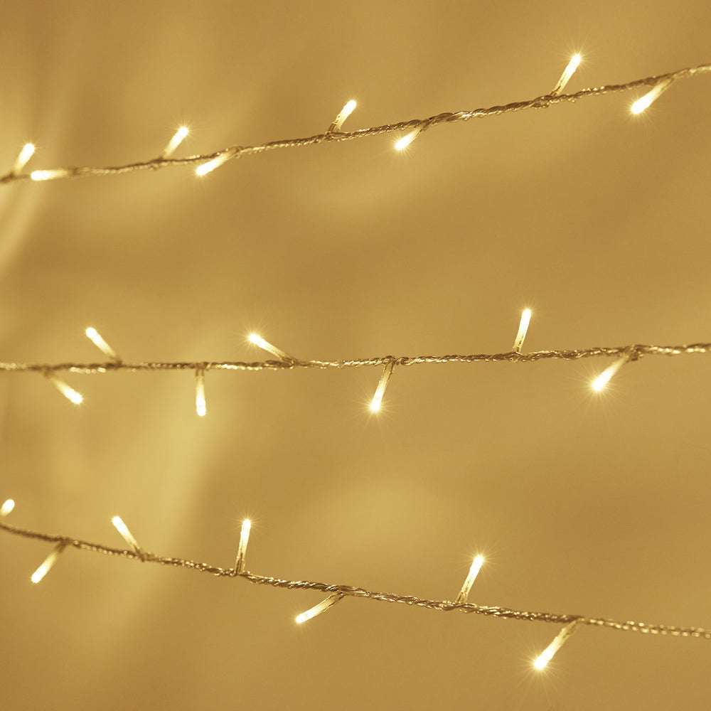 Nahaufnahme warmweiße LED-Lichterkette mit transparentem Kabel vor beigem Hintergrund