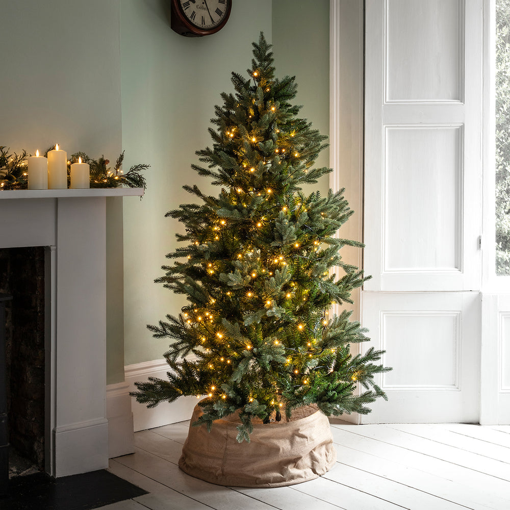 Weihnachtsbaum mit warmweißer LED-Lichterkette dekoriert neben Kamin und Fenster
