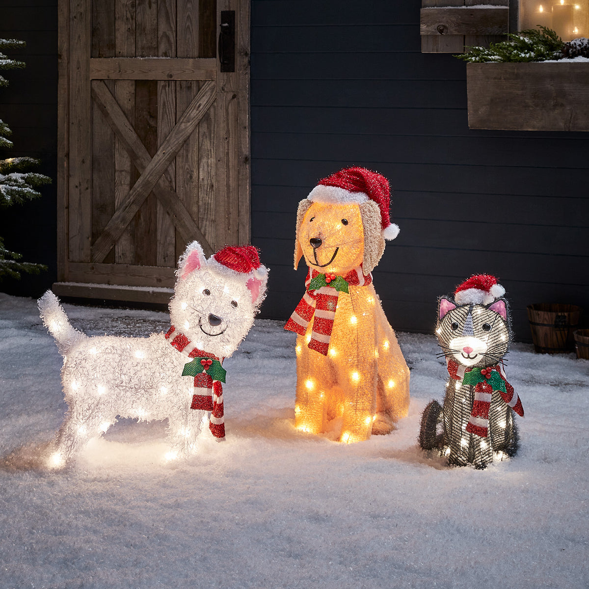 Beleuchtete Weihnachtsfiguren Labrador, Westie und Katze mit Mützen und Schals im Schnee vor Holztür