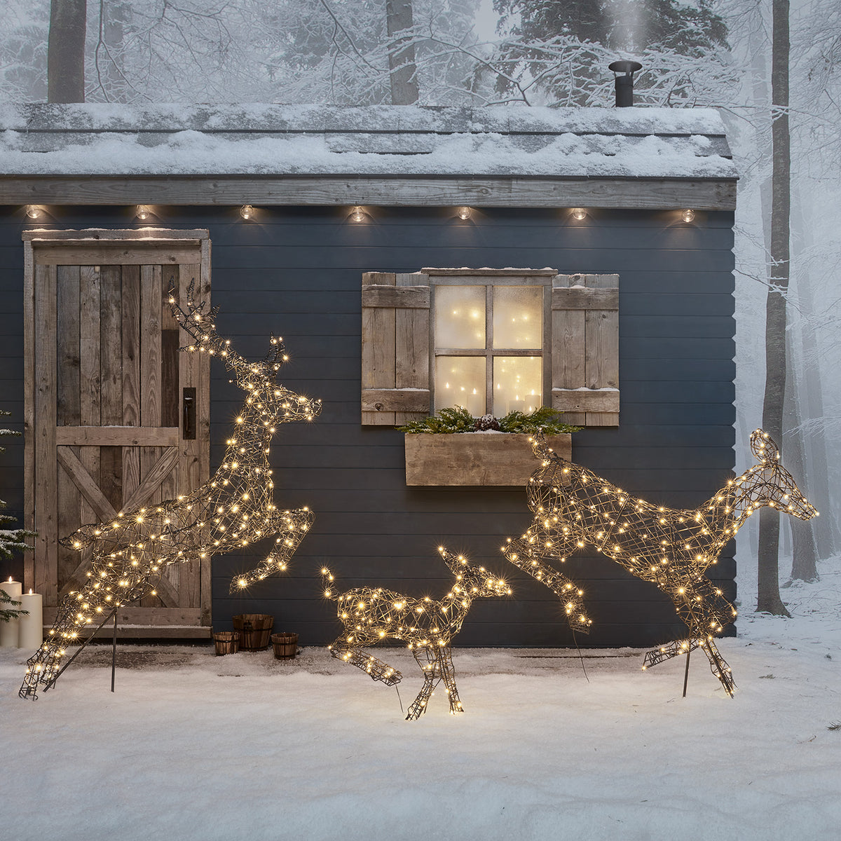 Drei springende LED-Rentiere mit warmweißen Lichtern vor Hausfassade im Schnee