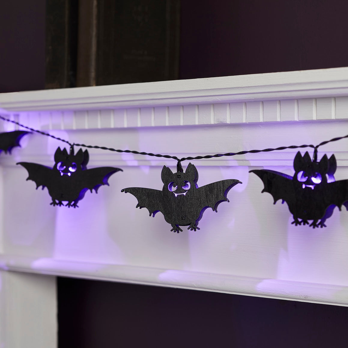Halloween Lichterkette mit schwarzen Holzfledermäusen und lila LEDs an weißem Kaminsims