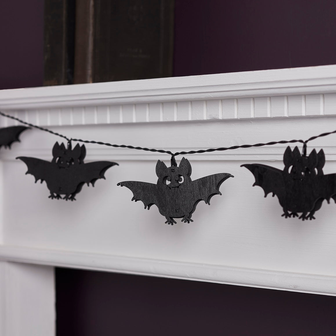Nahaufnahme der Halloween Lichterkette mit schwarzen Fledermäusen aus Holz an weißem Kaminsims