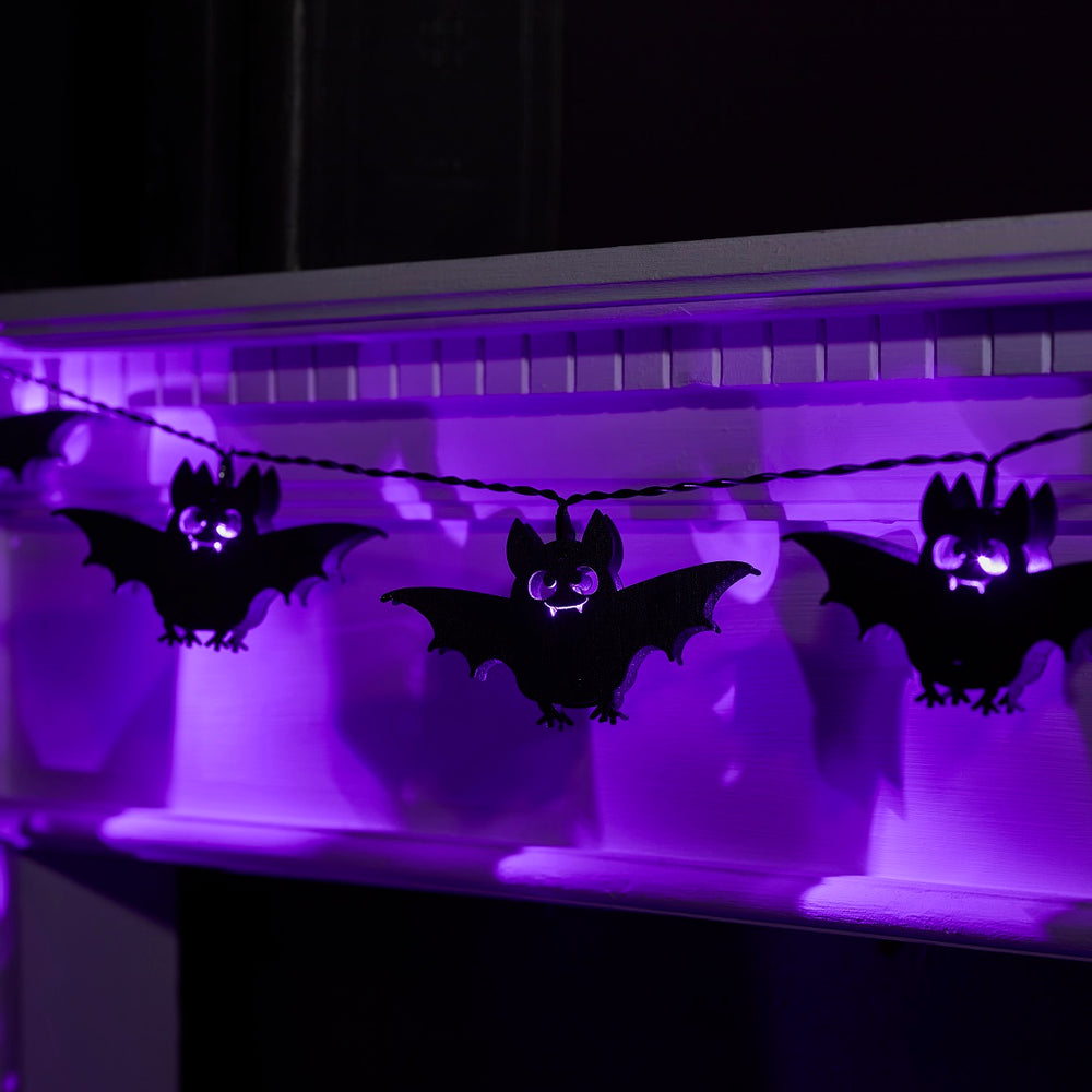 Dunkle Szene mit leuchtender Halloween Lichterkette aus Holzfledermäusen mit lila LEDs