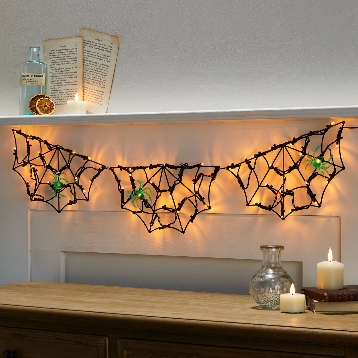 Halloween Lichterkette mit drei leuchtenden Spinnennetzen und grünen Spinnen an einem Kamin