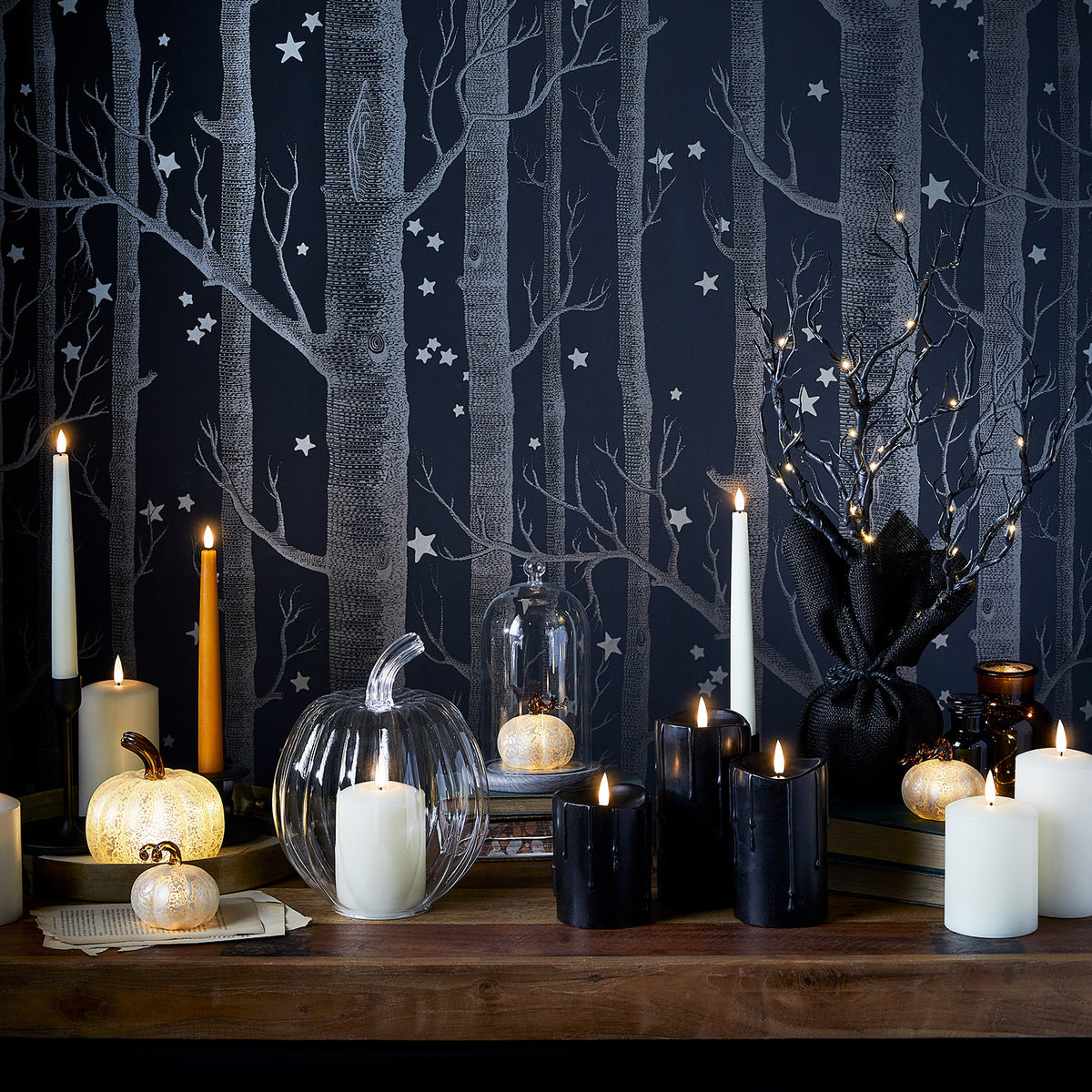 Halloween-Dekobaum mit LEDs umgeben von Kerzen und Kürbis-Deko vor schwarzer Waldtapete