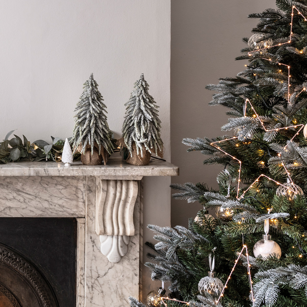 Zwei schneebedeckte Mini Weihnachtsbäume auf Kaminsims neben dekoriertem Weihnachtsbaum