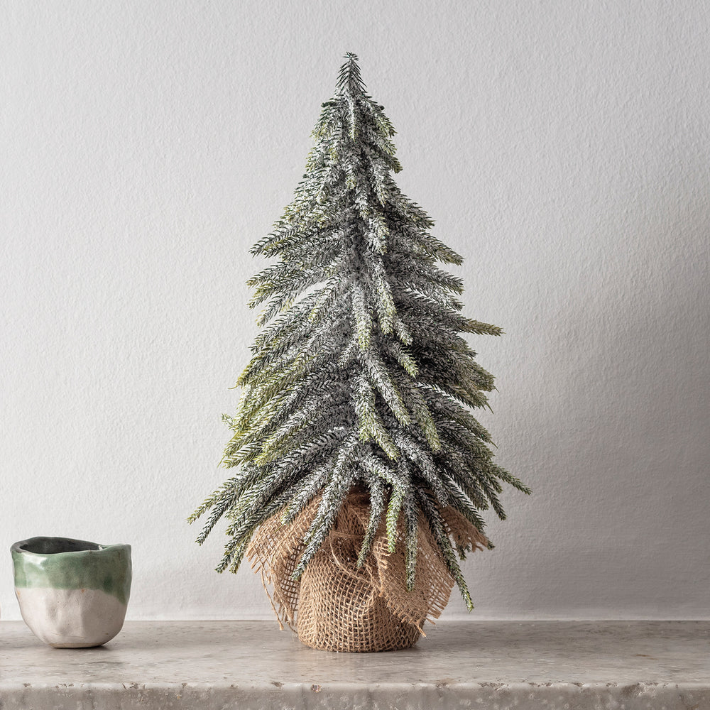 Schneebedeckter Mini Weihnachtsbaum mit Jutesack als Topf auf grauem Untergrund