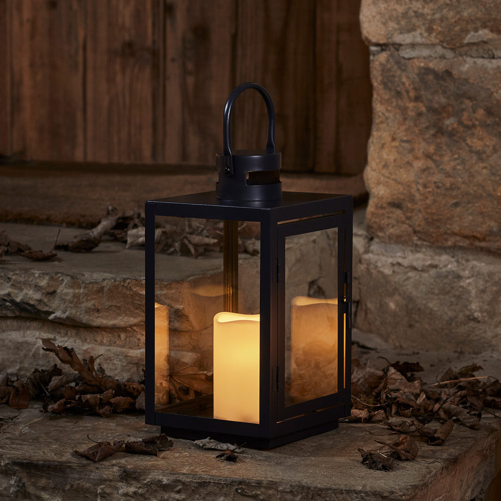 Schwarze LED Laterne mit warmweiß flackernder Kerze auf Steinboden vor Holztür