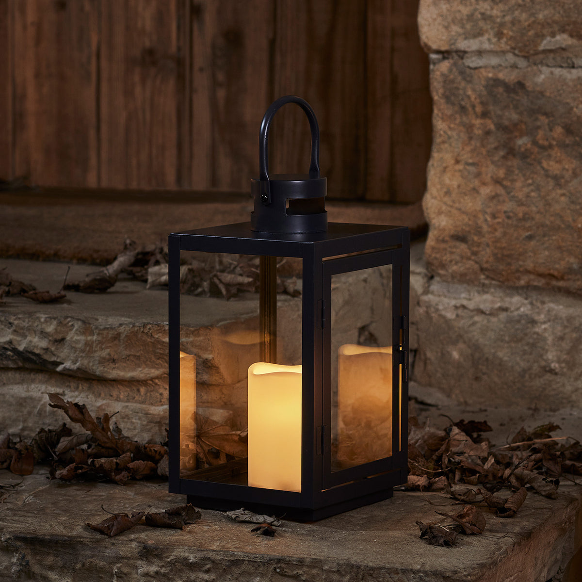 Schwarze LED Laterne mit warmweiß flackernder Kerze auf Steinboden vor Holztür