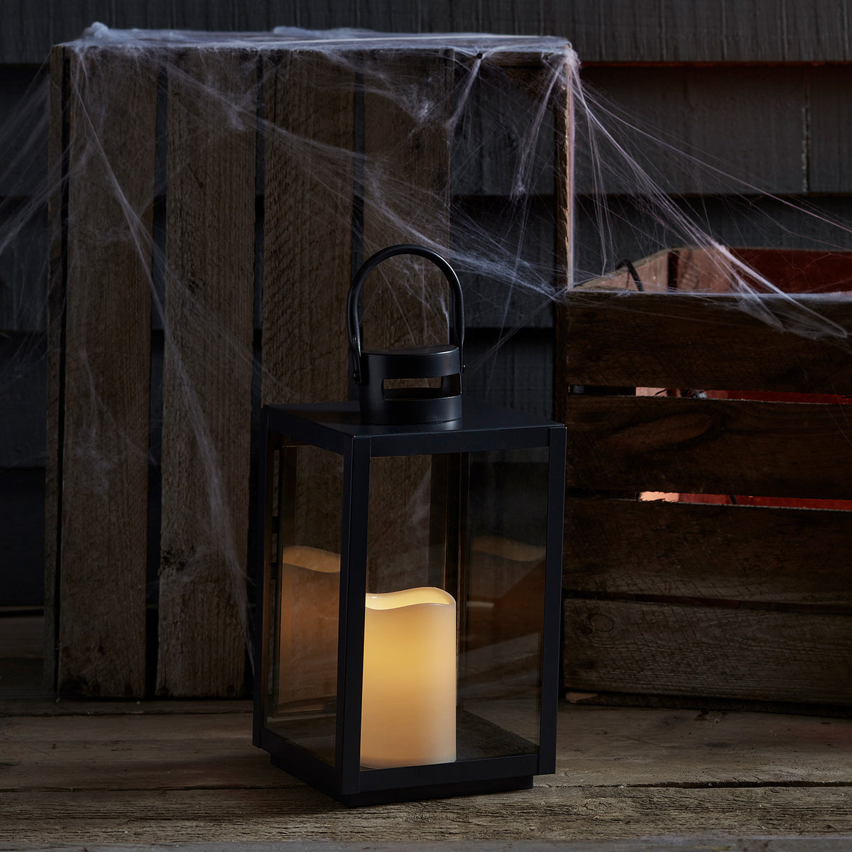 LED Laterne mit warmweißem Licht vor Holzkisten mit Spinnweben dekoriert