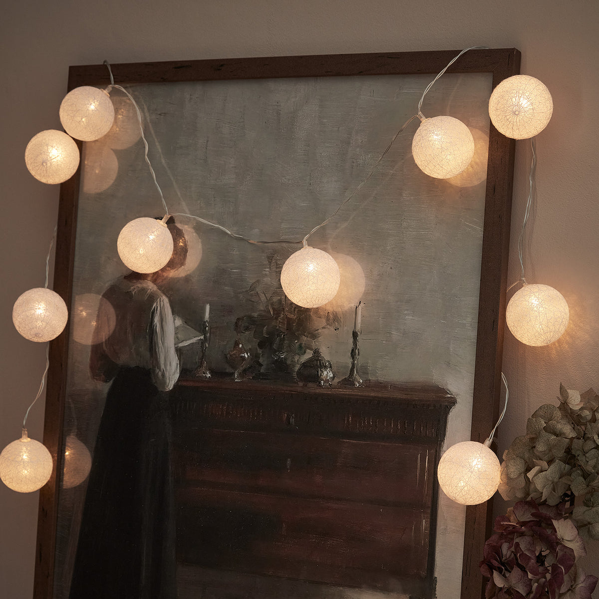 Weiße LED Cotton Ball Lichterkette mit 10 Kugeln vor einem gemalten Bild an der Wand