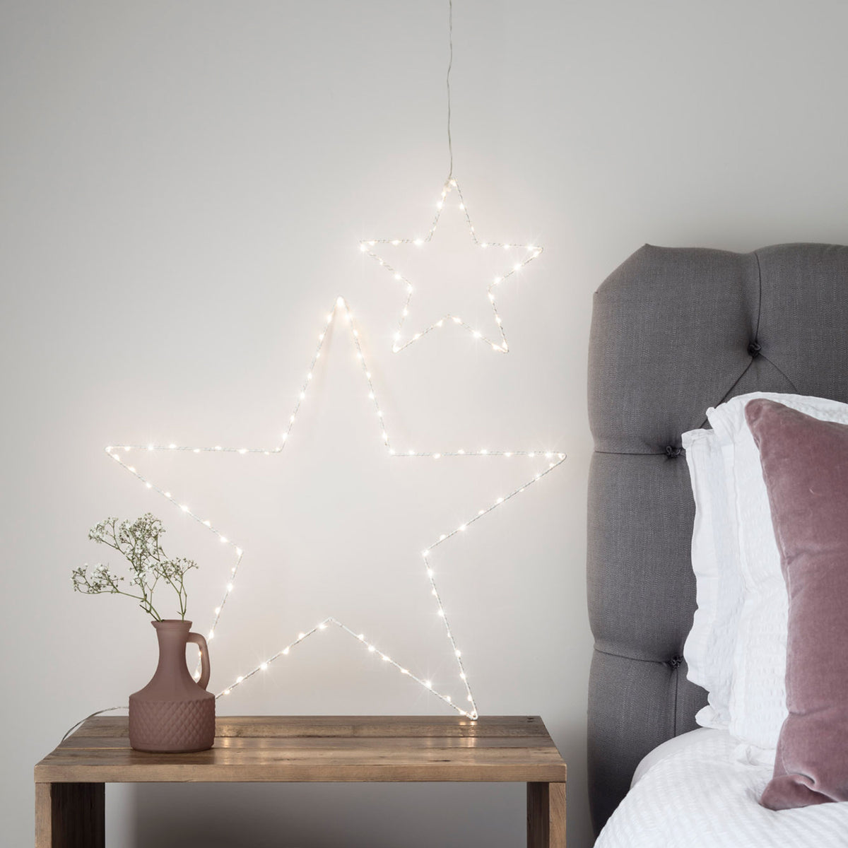 Weißer LED-Stern mit warmweißen LEDs auf Holztisch neben brauner Vase mit weißen Blumen