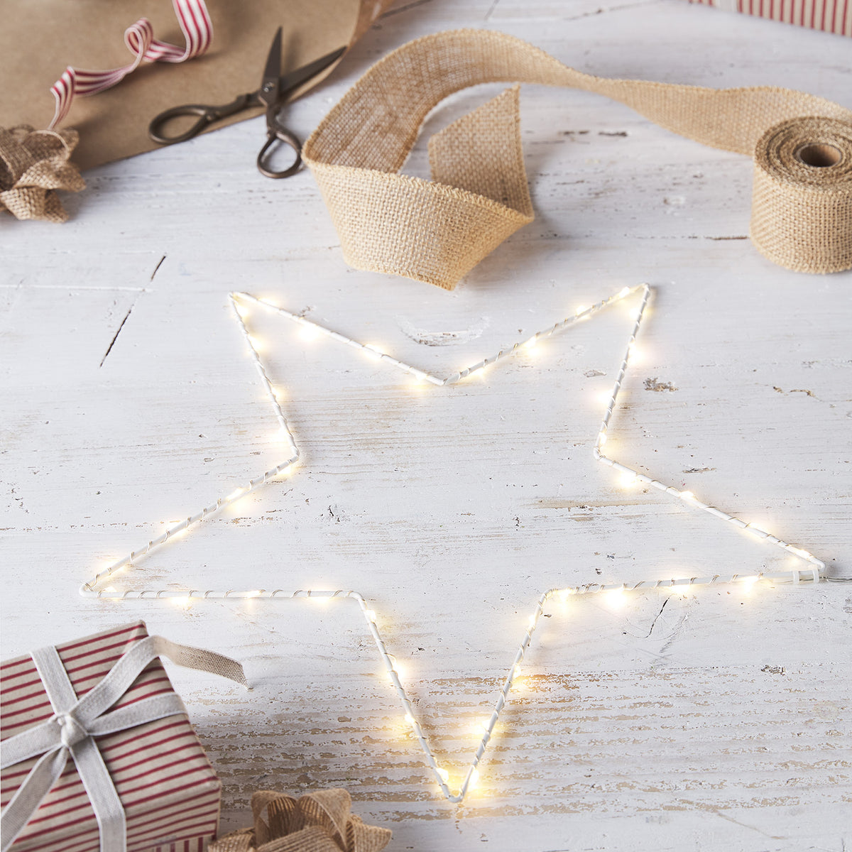 LED-Stern auf weißem Holztisch mit Geschenk, Geschenkband und Dekoschere