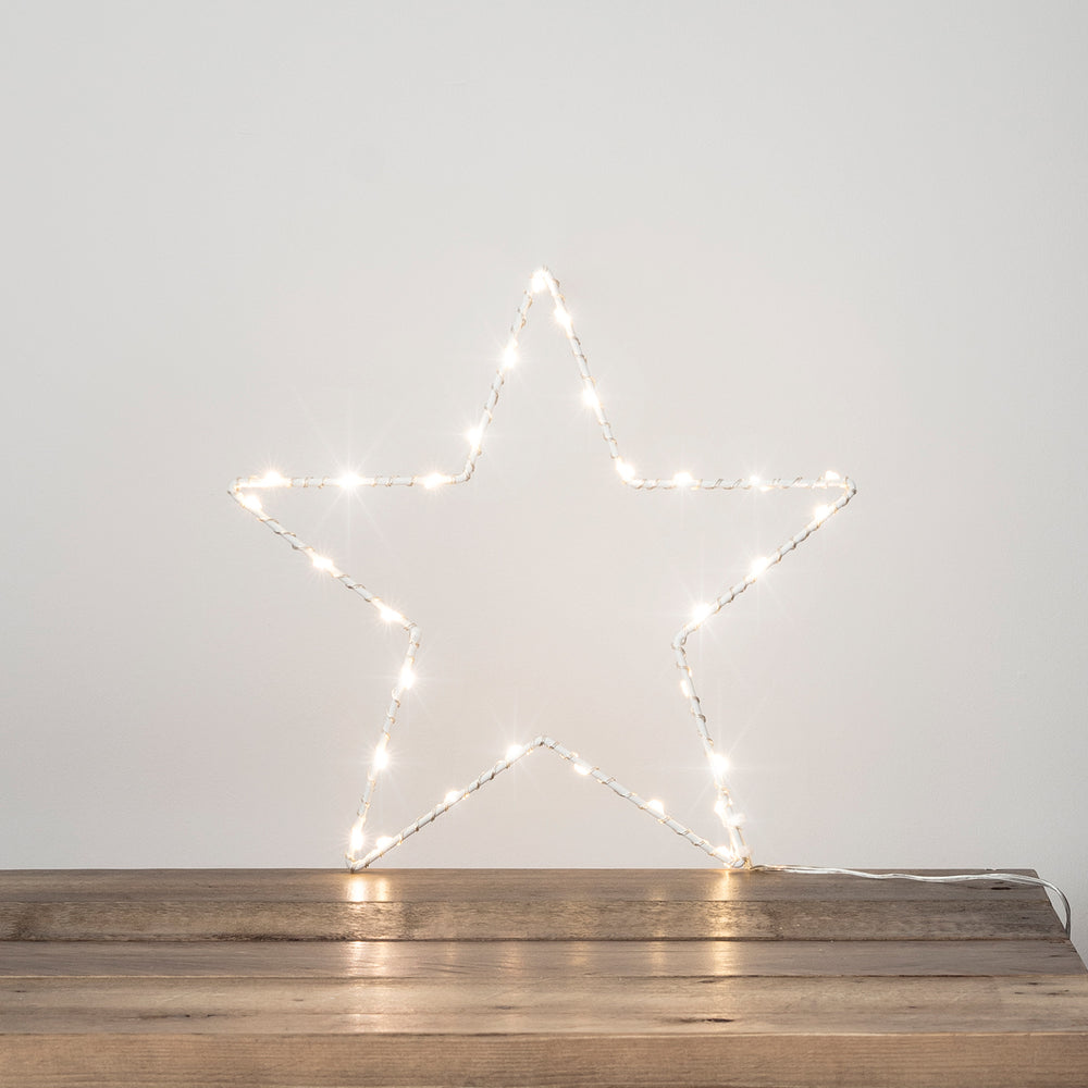 Weißer LED-Stern mit warmweißen Lichtern auf dunklem Holztisch vor heller Wand