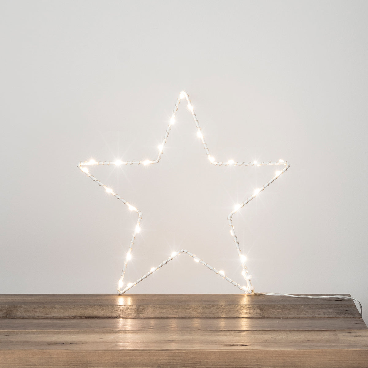 Weißer LED-Stern mit warmweißen Lichtern auf dunklem Holztisch vor heller Wand