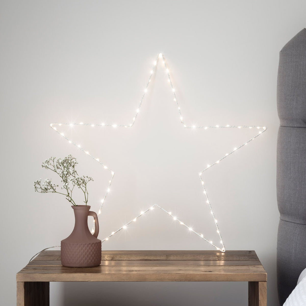 Leuchtender weißer LED-Stern mit warmweißen LEDs an Wand neben grauem Sofa und Kaminofen
