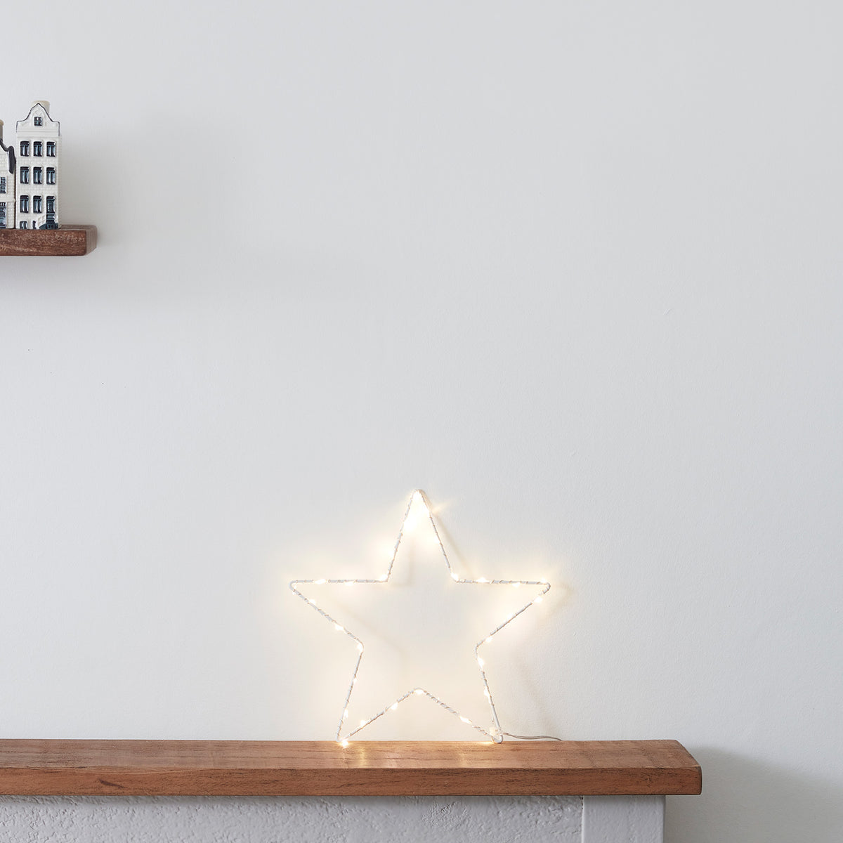 Leuchtender LED Stern auf Holztisch neben kleinen Keramikhäusern