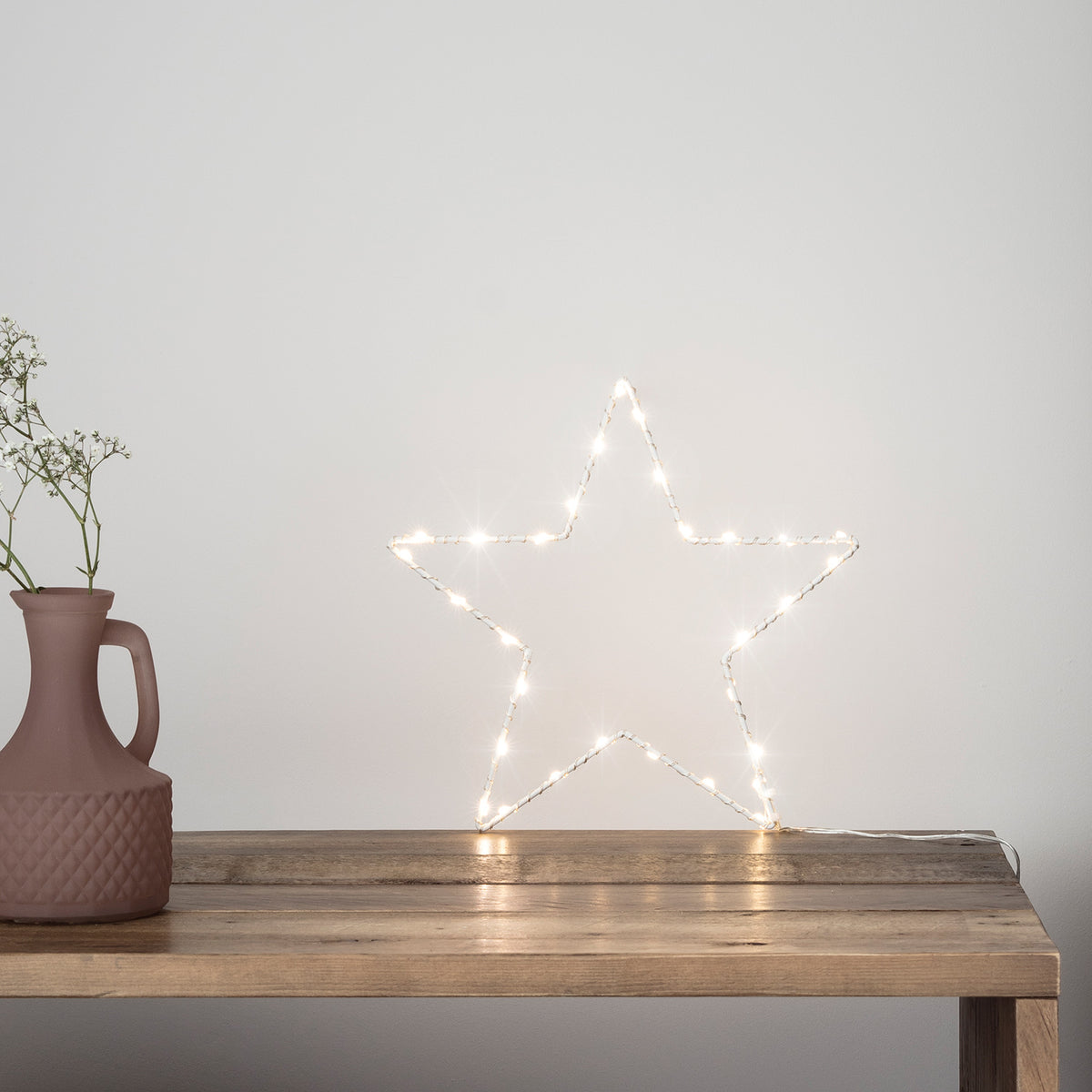 LED Stern auf Holztisch neben brauner Vase mit Zweigen