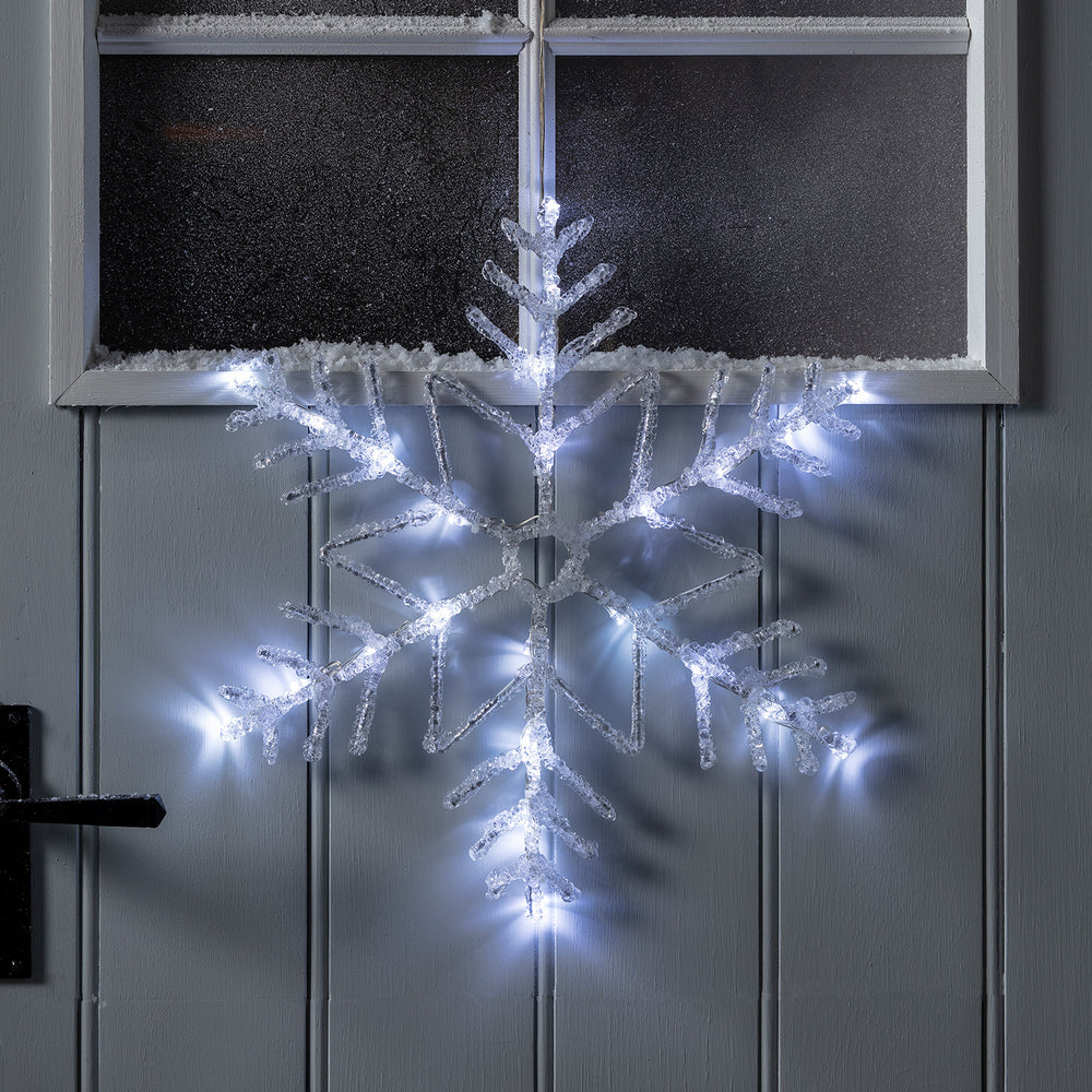 Beleuchtete LED-Schneeflocke an grauer Haustür mit Schnee auf Fensterrahmen