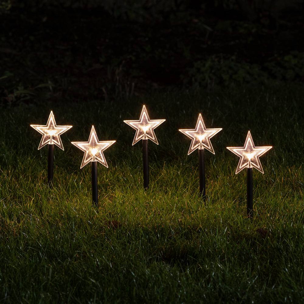 Fünf leuchtende Sternen-Stableuchten mit warmweißen LEDs im Garten bei Nacht