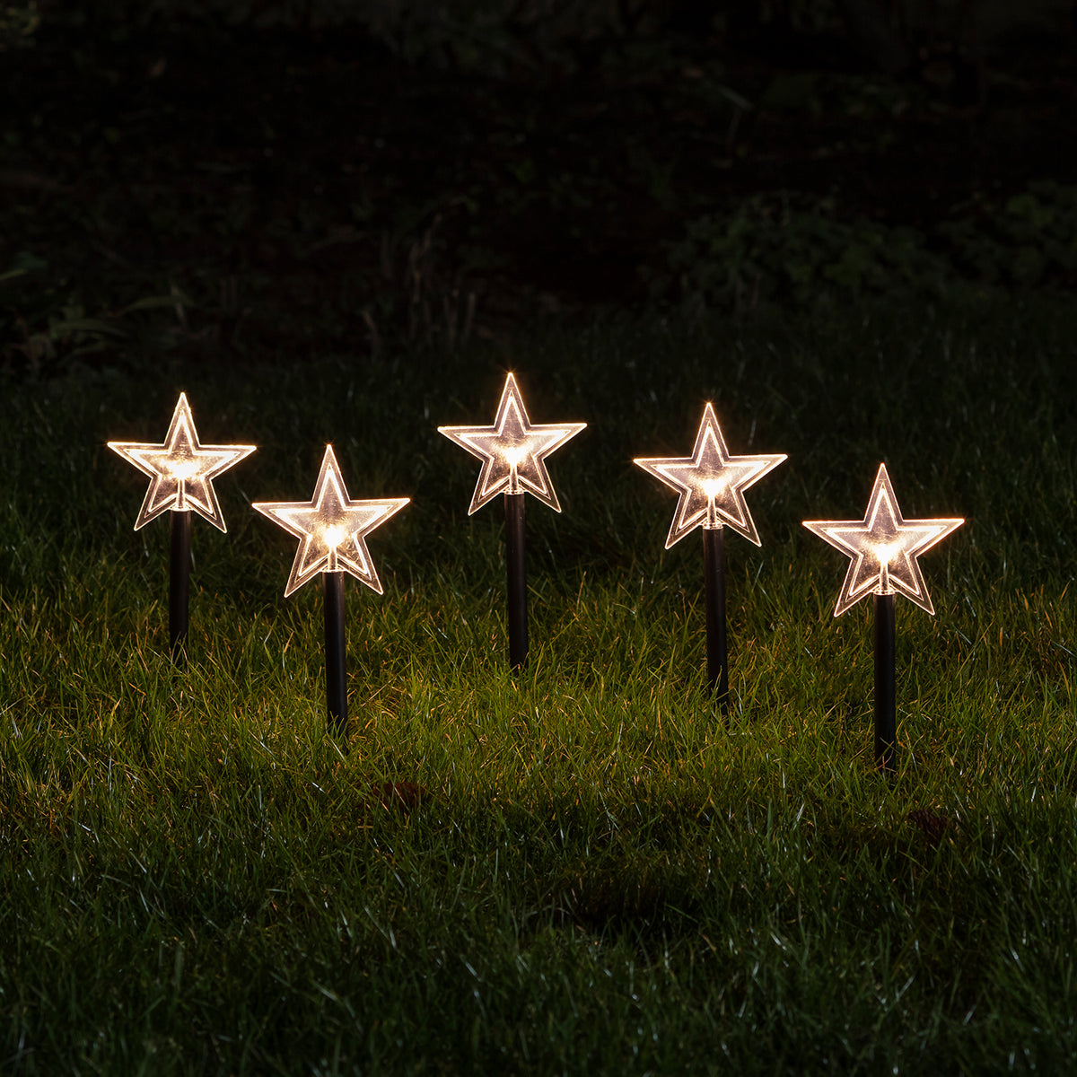 Fünf leuchtende Sternen-Stableuchten mit warmweißen LEDs im Garten bei Nacht